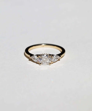 handcrafted white diamond engagement ring featuring large cushion cut center stone accented with two pear shaped stones set in 14k yellow gold band macha studio brooklyn new york
