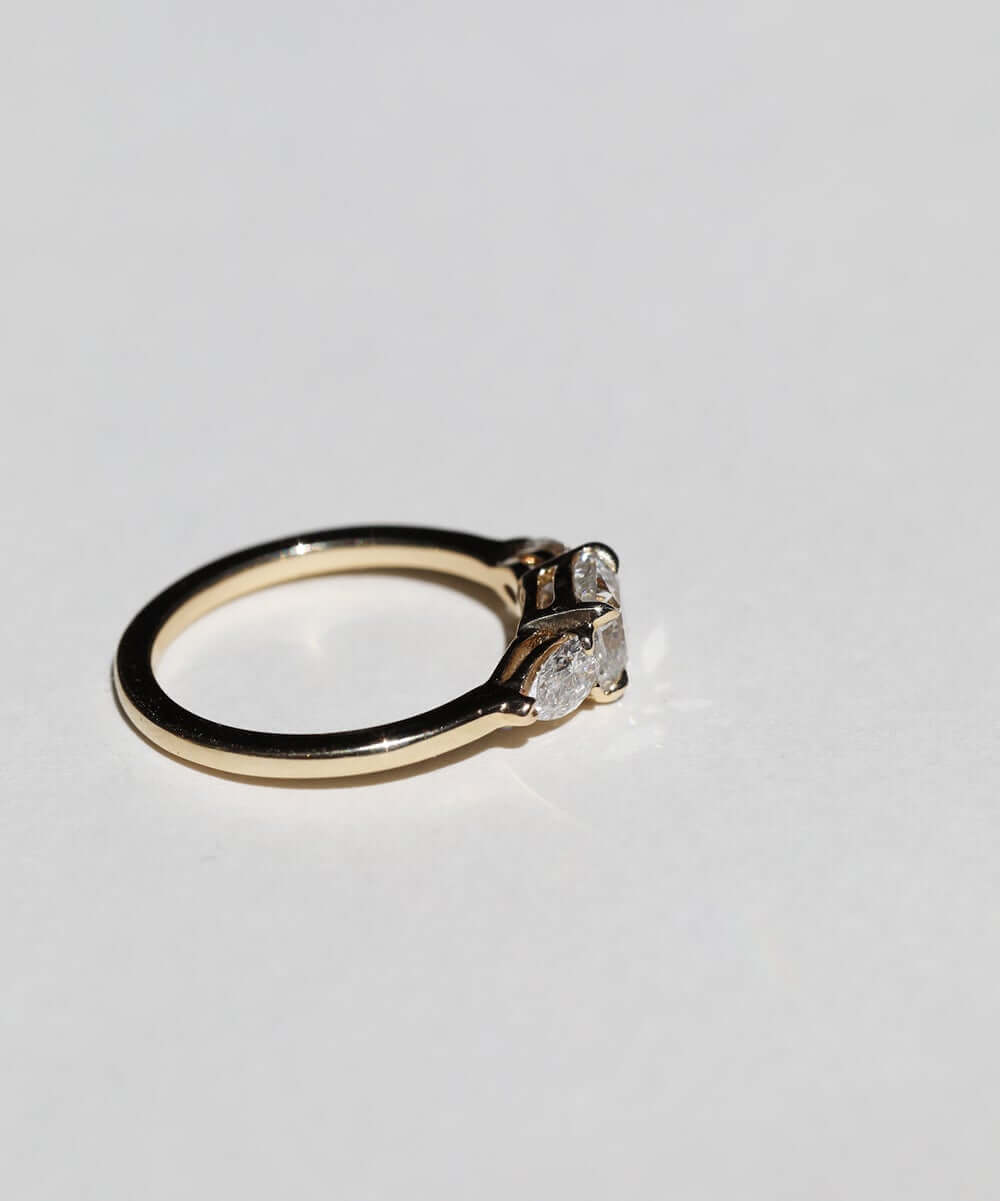 handcrafted white diamond engagement ring featuring large cushion cut center stone accented with two pear shaped stones set in 14k yellow gold band macha studio brooklyn new york