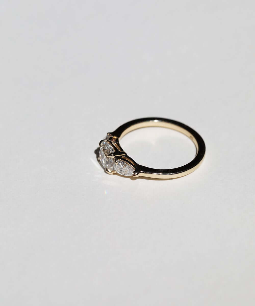 handcrafted white diamond engagement ring featuring large cushion cut center stone accented with two pear shaped stones set in 14k yellow gold band macha studio brooklyn new york
