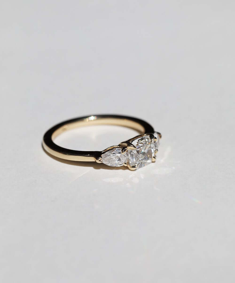 handcrafted white diamond engagement ring featuring large cushion cut center stone accented with two pear shaped stones set in 14k yellow gold band macha studio brooklyn new york