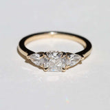 handcrafted white diamond engagement ring featuring large cushion cut center stone accented with two pear shaped stones set in 14k yellow gold band macha studio brooklyn new york