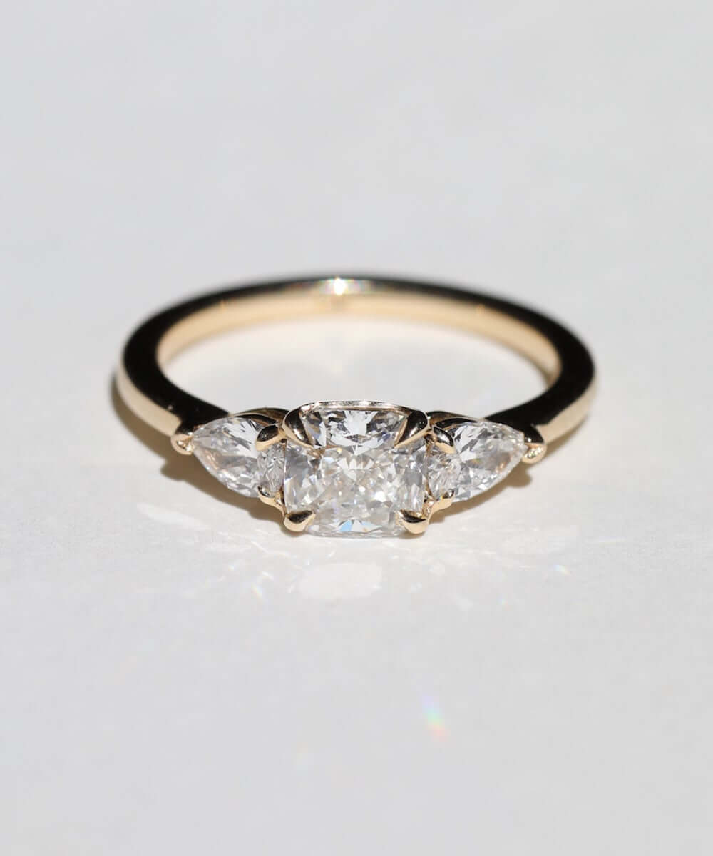 handcrafted white diamond engagement ring featuring large cushion cut center stone accented with two pear shaped stones set in 14k yellow gold band macha studio brooklyn new york