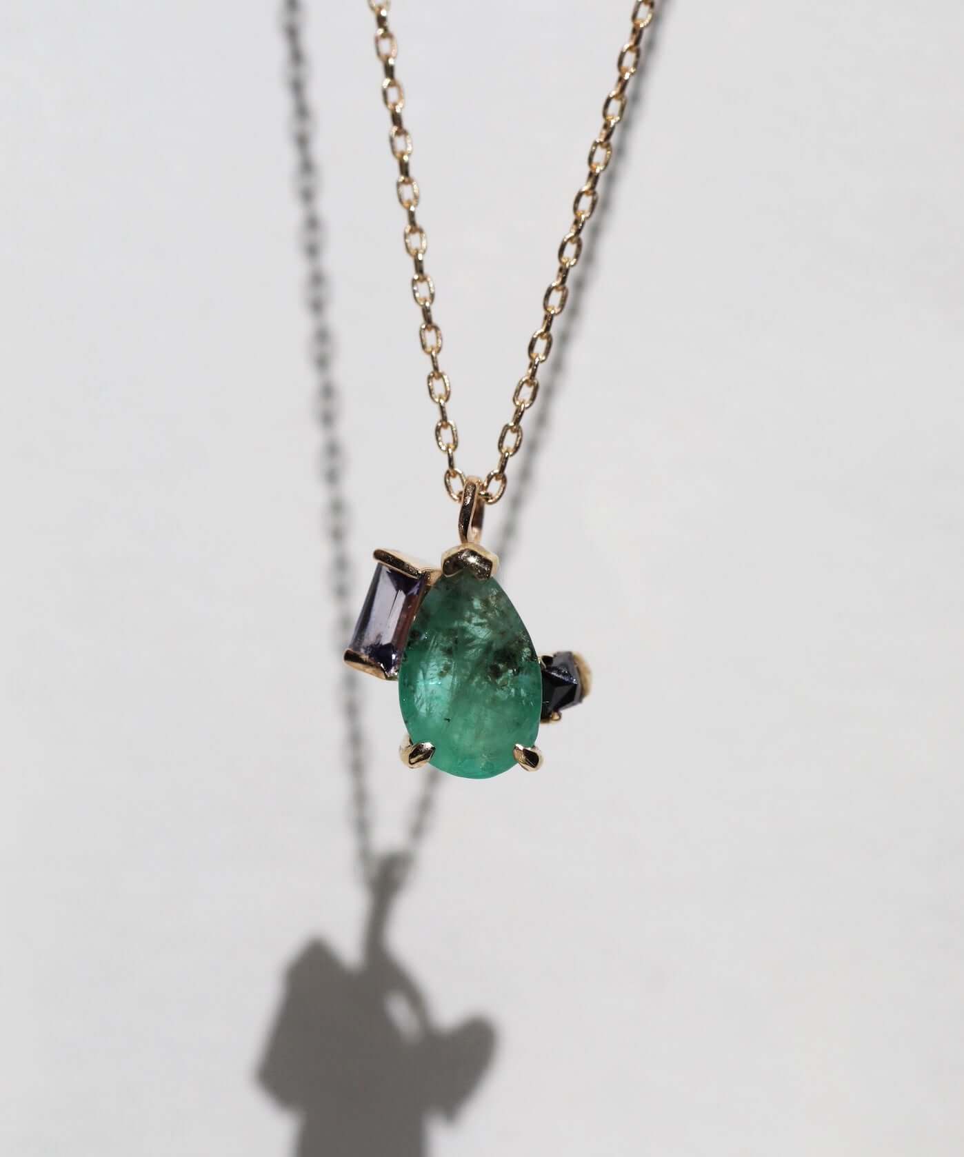 Pear shaped emerald with peppery textures, combined with a purple sapphire and an inverted black emerald cut diamond, 14k gold, 18" chain